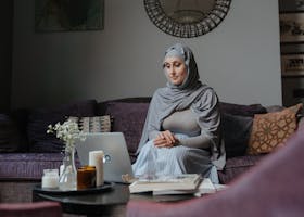 Middle Eastern woman sitting on a sofa working on a laptop in a living room setting.